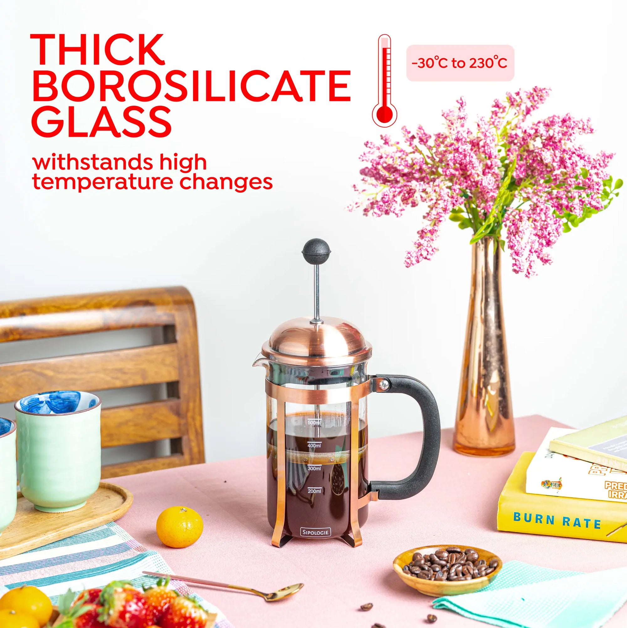 A copper-finished and borosilicate glass French press coffee maker sits on a pink tablecloth in a styled kitchen scene with flowers, a wooden chair, and coffee accessories. Large text on the left reads 'THICK BOROSILICATE GLASS' and 'withstands high temperature changes' with a temperature range badge.
