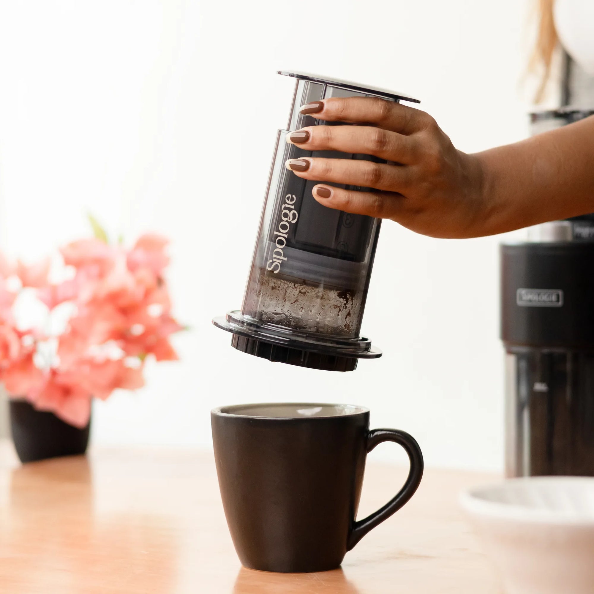 Hand holding a Sipologie coffee maker over a black mug on a blurred kitchen background