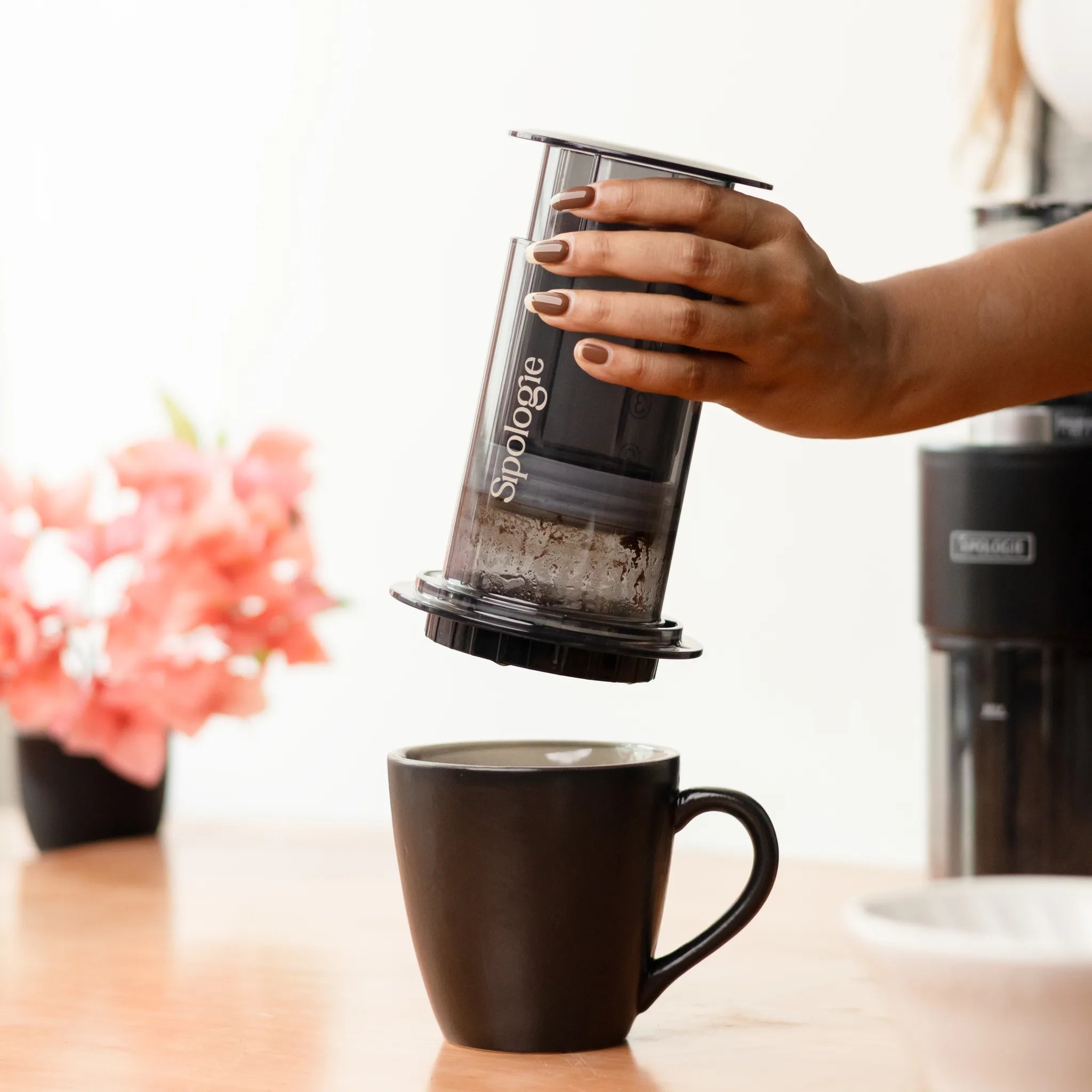 Hand holding a Sipologie coffee maker over a black mug on a blurred kitchen background