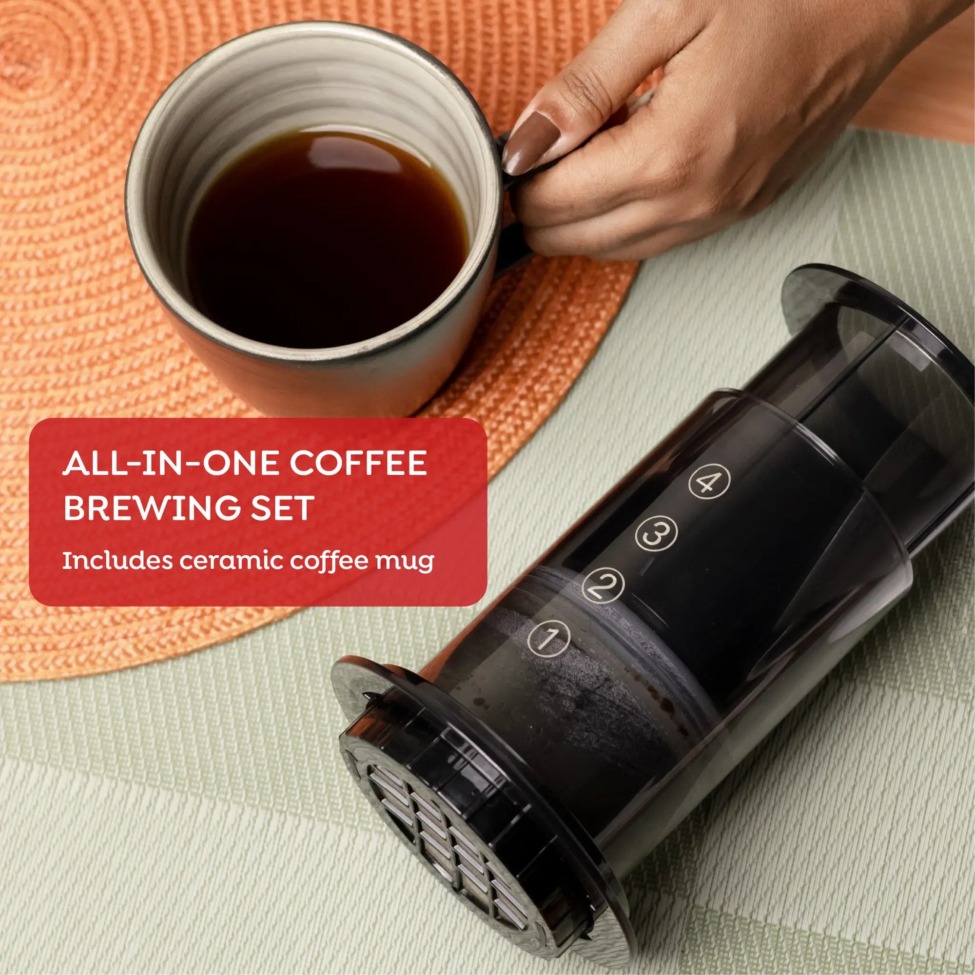 All-in-one coffee brewing set with a ceramic coffee mug on an orange mat.
