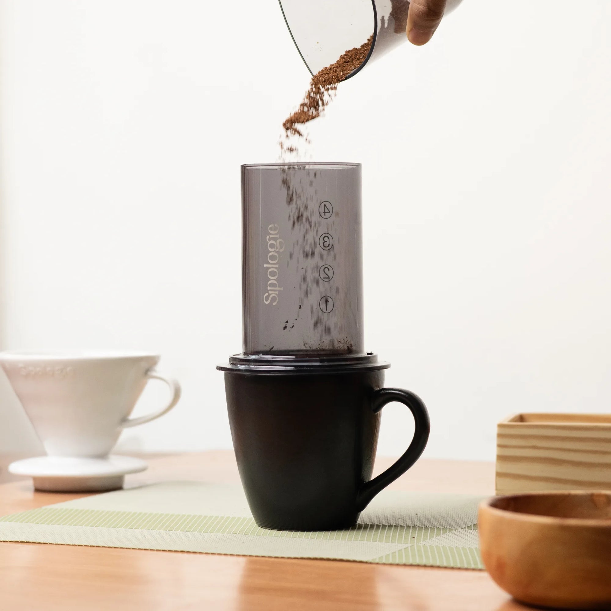 Coffee grinder being used to grind coffee beans into a black mug on a wooden table.