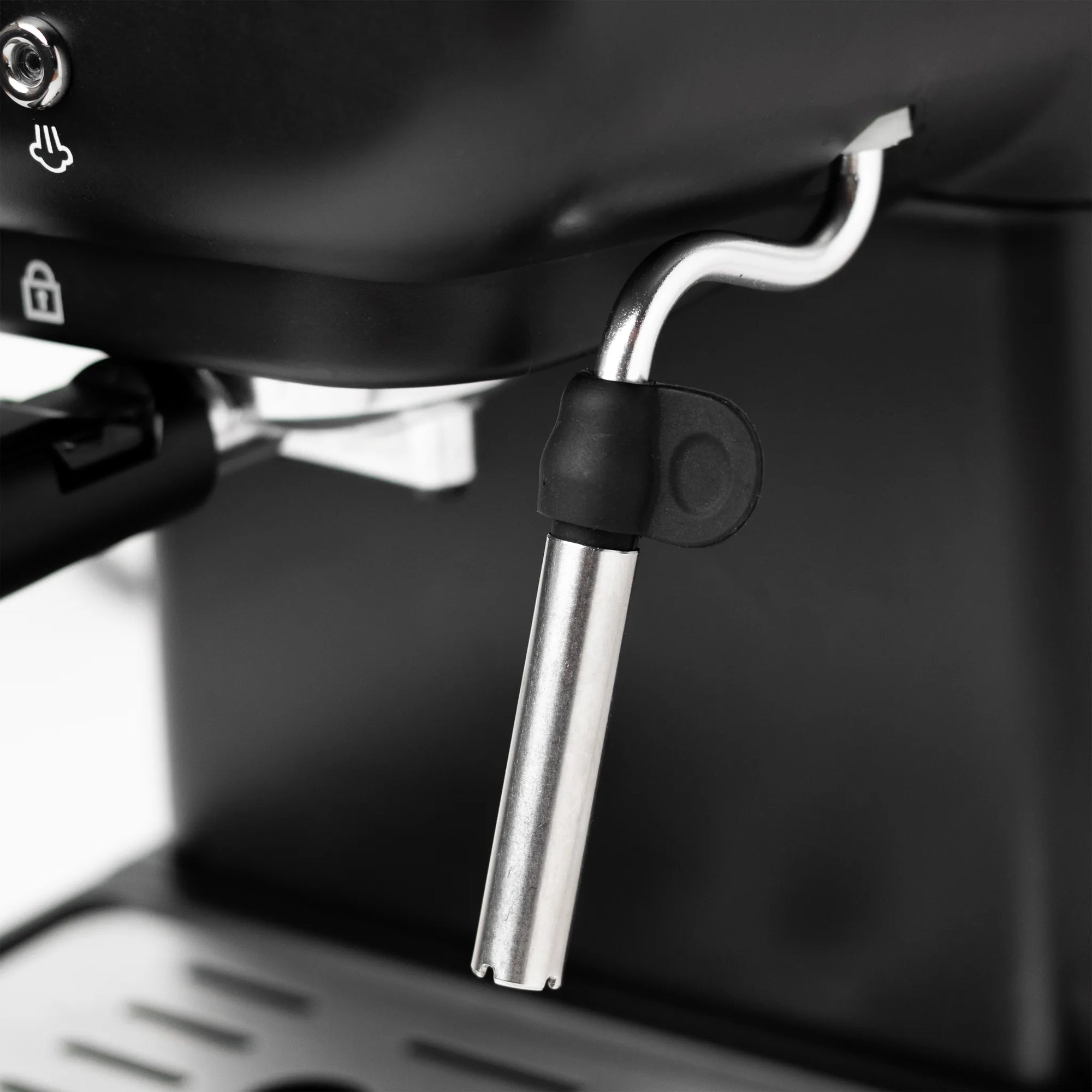 Close-up of a metallic steam wand attachment with a black protective sleeve, mounted near the steam release valve of a black espresso machine.