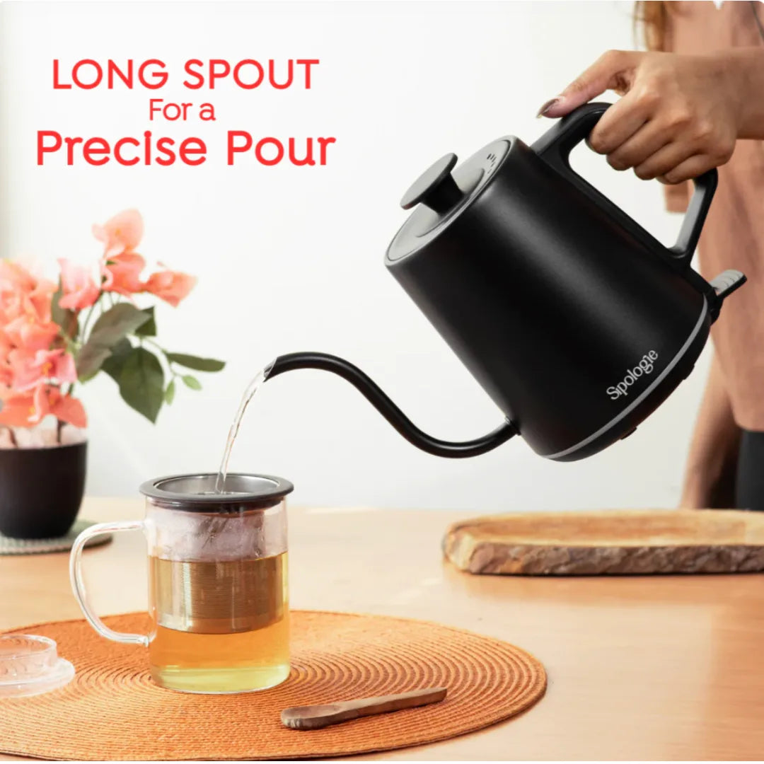 A person pours hot water from a matte black gooseneck kettle into a glass mug with a metal infuser, set on a wooden table with a woven placemat. Red text in the upper left reads 'LONG SPOUT For a Precise Pour'.