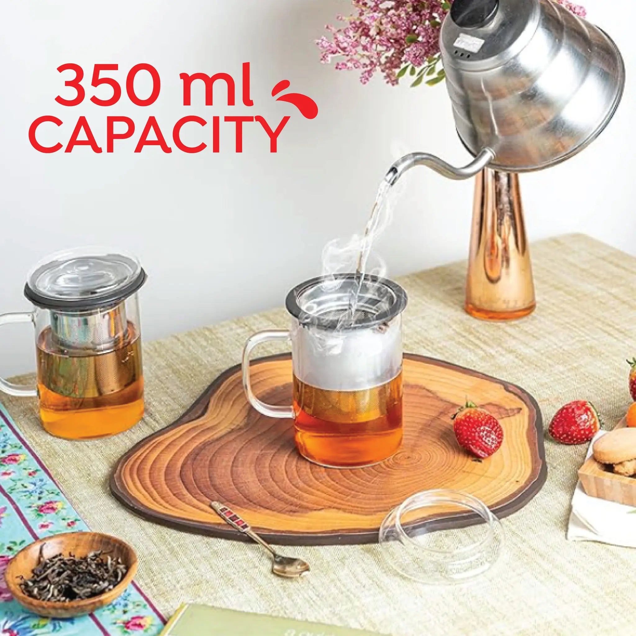 A clear glass teapot with a metal infuser and handle sits on a wooden tray beside a copper kettle pouring hot water into it. Red text in the upper left reads '350 ml CAPACITY'.