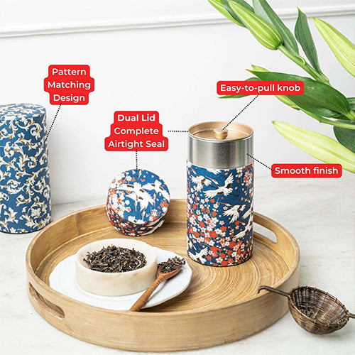 A tea storage set displayed on a round wooden tray, including a tall patterned container, a smaller matching container, a lid, a bowl of loose tea, a wooden spoon, and a metal tea strainer. Red callout labels point to features such as pattern matching design, dual lid complete airtight seal, easy-to-pull knob, and smooth finish.