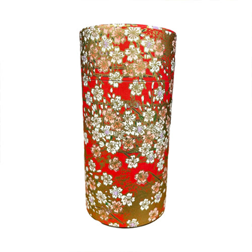 A cylindrical metal tea canister decorated with a traditional Japanese floral pattern featuring white and pink blossoms on a red and gold background, isolated on a white background.