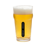 A clear pint glass filled with golden beer and topped with white foam, featuring a vertical black label that reads 'YOUR NAME' in white text, isolated on a white background.