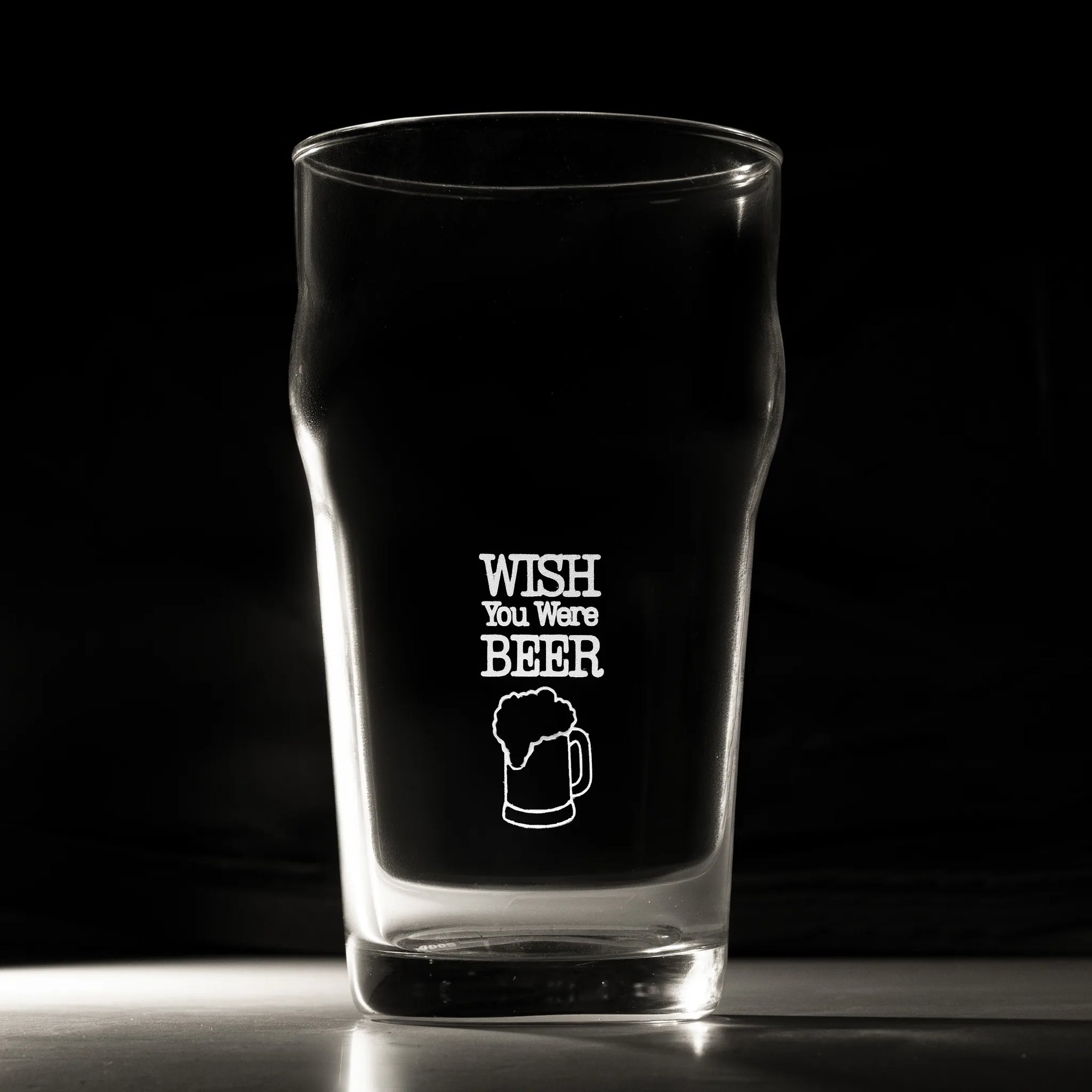 Clear glass pint glass with 'Wish You Were Beer' text and graphic on a black background
