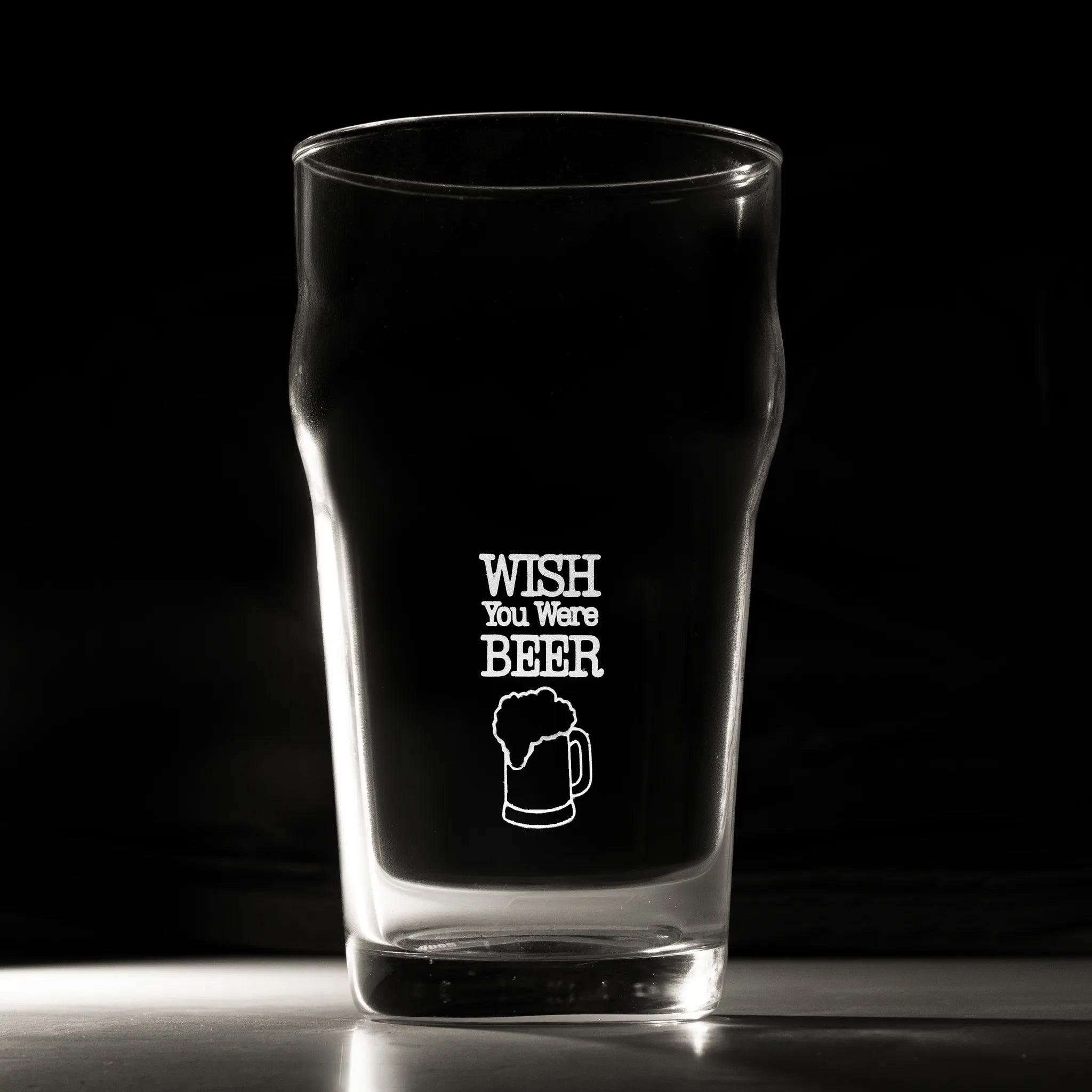 Clear glass pint glass with 'Wish You Were Beer' text and graphic on a black background